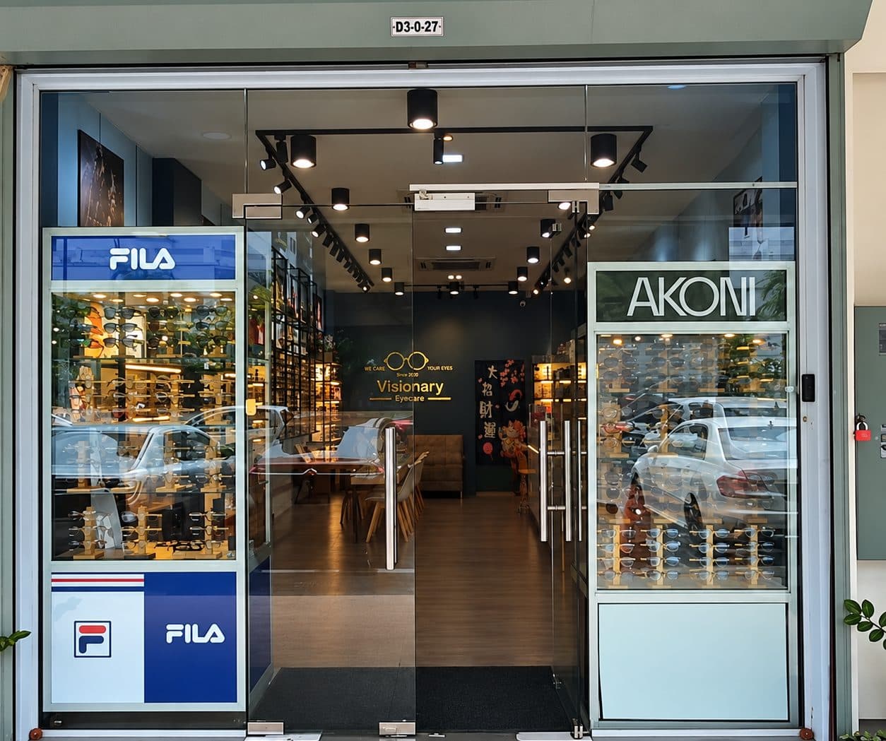 The glass entrance of Visionary Eyecare at unit D3-0-27, with FILA and AKONI frame displays either side of the door