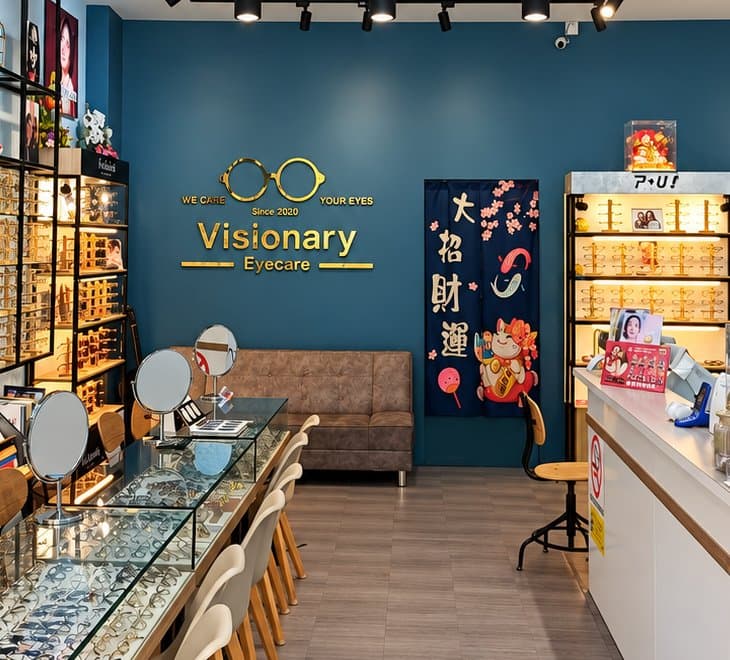 The navy logo wall inside Visionary Eyecare at OUG Parklane, with the gold "We care your eyes" logo above a sofa